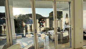 A modern living room with a large sliding glass door leading to a balcony. There is a white sofa with a cushion and a fan on the floor. - Luxurious sea view villa for 6 people, 1km from the beach (Marbella)