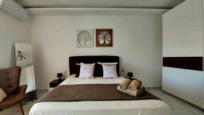 A bedroom with a large bed, two pillows, a blanket, and a chair. There are two wall-mounted artworks above the bed. - Penthouse with Private Roof Top Pool (Ix-Xaghra)