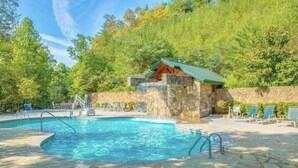 Una piscina con cubierta de piedra, sillas de descanso y un edificio de techo verde.