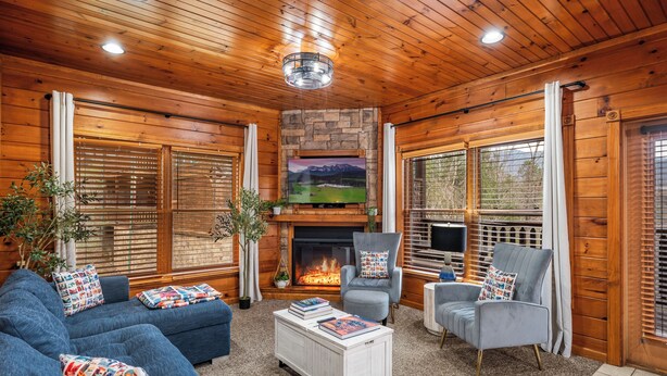 Una sala de estar acogedora con chimenea, paredes de madera y ventanas amplias.