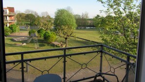 A balcony with a view of a park, including a playground and trees.