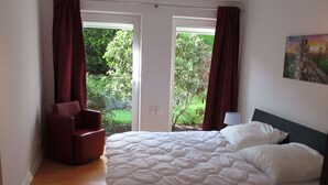 A bedroom with a bed, a chair, and a view of greenery through a door.