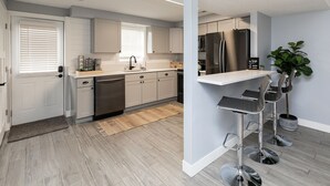 A modern kitchen with white cabinets, stainless steel appliances, and a bar area with stools. - A Private Boho-Modern Stay Minutes to Downtown w/ KING Bed and Hidden Nook! (Des Moines)
