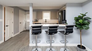 A modern kitchen with a white countertop, black bar stools, and a potted plant. - A Private Boho-Modern Stay Minutes to Downtown w/ KING Bed and Hidden Nook! (Des Moines)