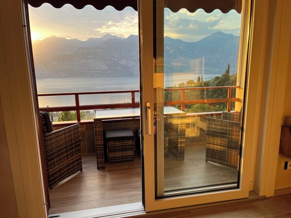 Un balcon agrémenté de meubles en osier, avec vue sur un lac et des montagnes à l’horizon.