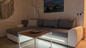 A modern living room with a sofa, a small wooden table, a wall-mounted TV, and a framed picture of a coastal town. - Casa di Alessia THE new vacation apartment with dream view over Malcesine incl. pool (Malcesine)