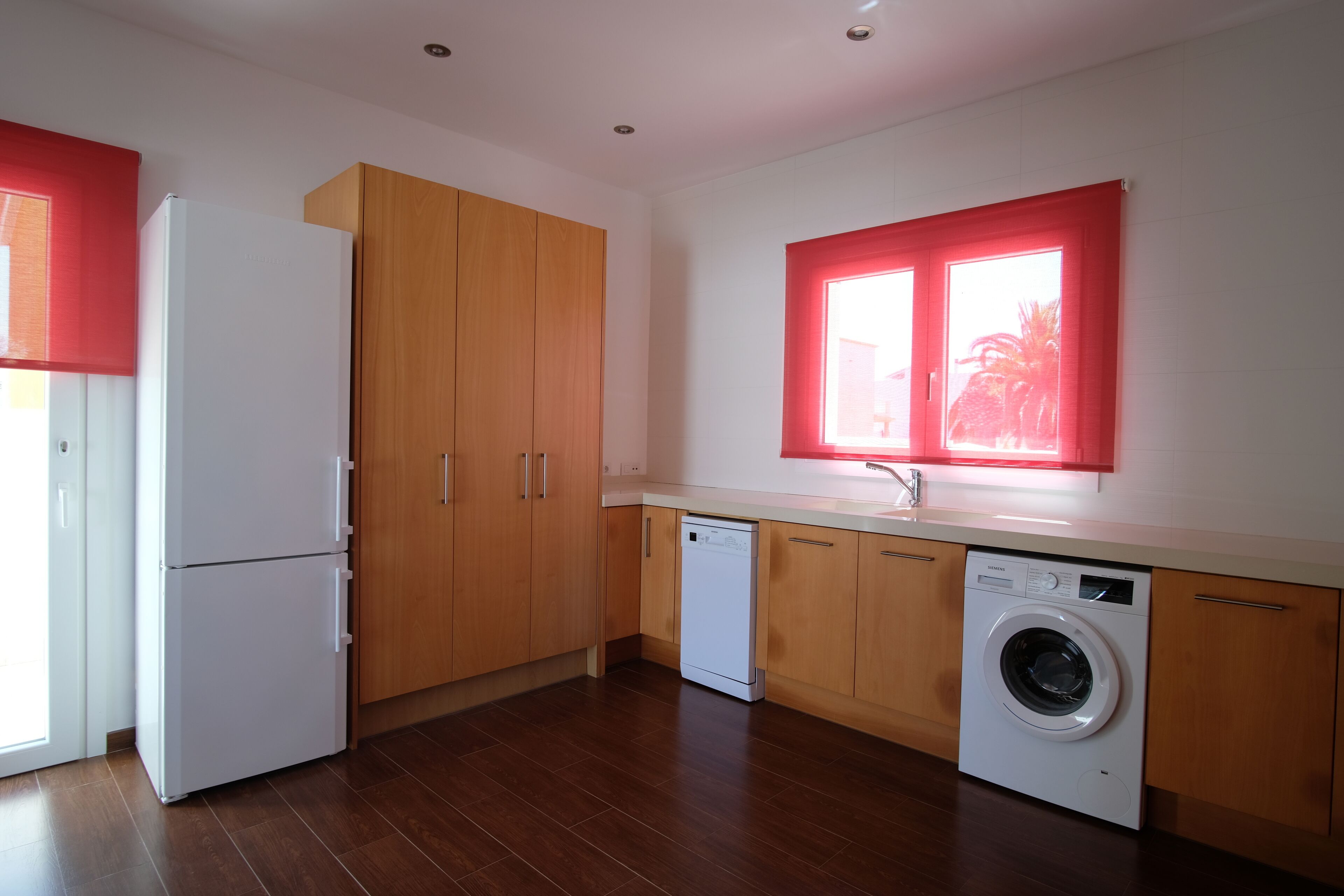 A kitchen with wooden cabinets, a white refrigerator, a dishwasher, and a washing machine.