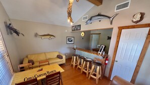 Zona d'estar acollidora amb taula de dinar de fusta amb el lema 'Chill Canyon Ranch', un sofà de cuir i una barra amb tamborets.