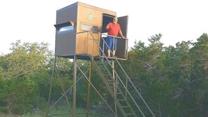 Un home al capdamunt d'una escala metàl·lica que condueix a un torre d'observació de fusta amb una porta oberta.