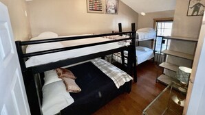 Habitació amb literes, ventilador de sostre, finestra i una taula petita amb làmpada.