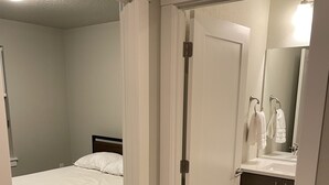 A bedroom with a single bed, a bathroom with a sink and mirror, and a carpeted floor. - Comfy Cool Condo 5min from McMenamins Edgefield &10min from Columbia River Gorge (Troutdale)