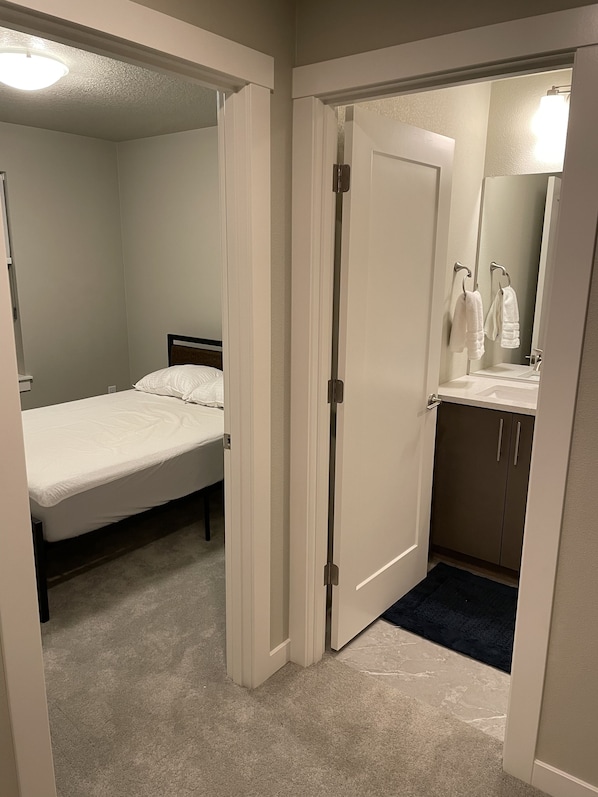 Un dormitorio con una cama individual, un baño con lavamanos y espejo, y piso alfombrado.