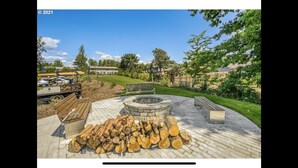 A patio area with a fire pit, a stack of firewood, and a bench. - Comfy Cool Condo 5min from McMenamins Edgefield &10min from Columbia River Gorge (Troutdale)