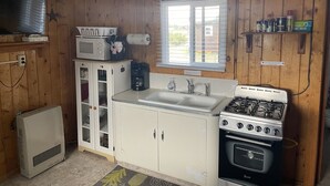 A compact kitchen with wooden walls, a microwave, a stove, a sink, and a small window. - Cozy cabin #1 in mountains near Rio Grande River (South Fork)