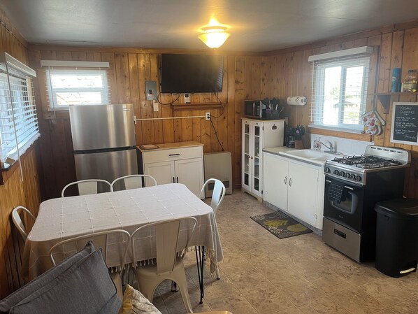 A compact kitchen with a dining table, chairs, a refrigerator, a microwave, a stove, and a television.
