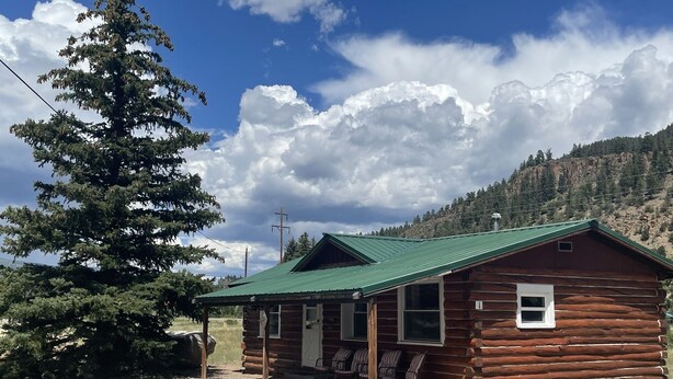 A rustic log cabin with a green roof, a porch with chairs, and a view of a mountainous landscape. - Cozy cabin #1 in mountains near Rio Grande River (South Fork)