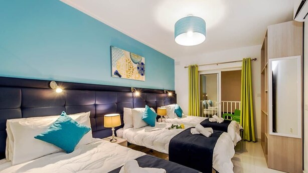 Ein Hotelzimmer mit zwei Betten, einem großen Kopfteil, einem Gemälde an der Wand und Blick ins Freie durch ein Fenster.