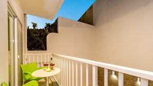 Ein Balkon mit weißer Reling, einem runden Tisch und zwei grünen Stühlen.