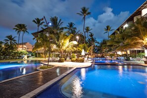 A resort pool area with palm trees, lounge chairs, and a wooden deck.