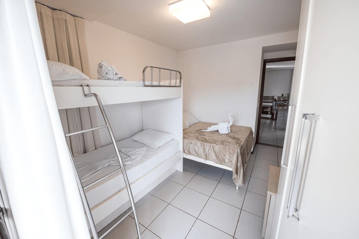 Quarto tipo dormitório com beliches, uma mesa pequena e uma cadeira.