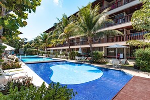 Relax by the resort's large pool surrounded by lush greenery and palm trees, with lounge chairs and umbrellas at your disposal.