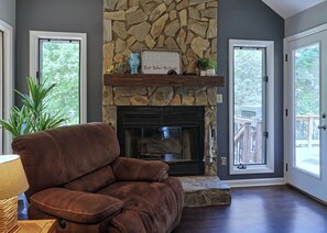 A living room with a stone fireplace, a brown leather chair, and a view through the glass doors.