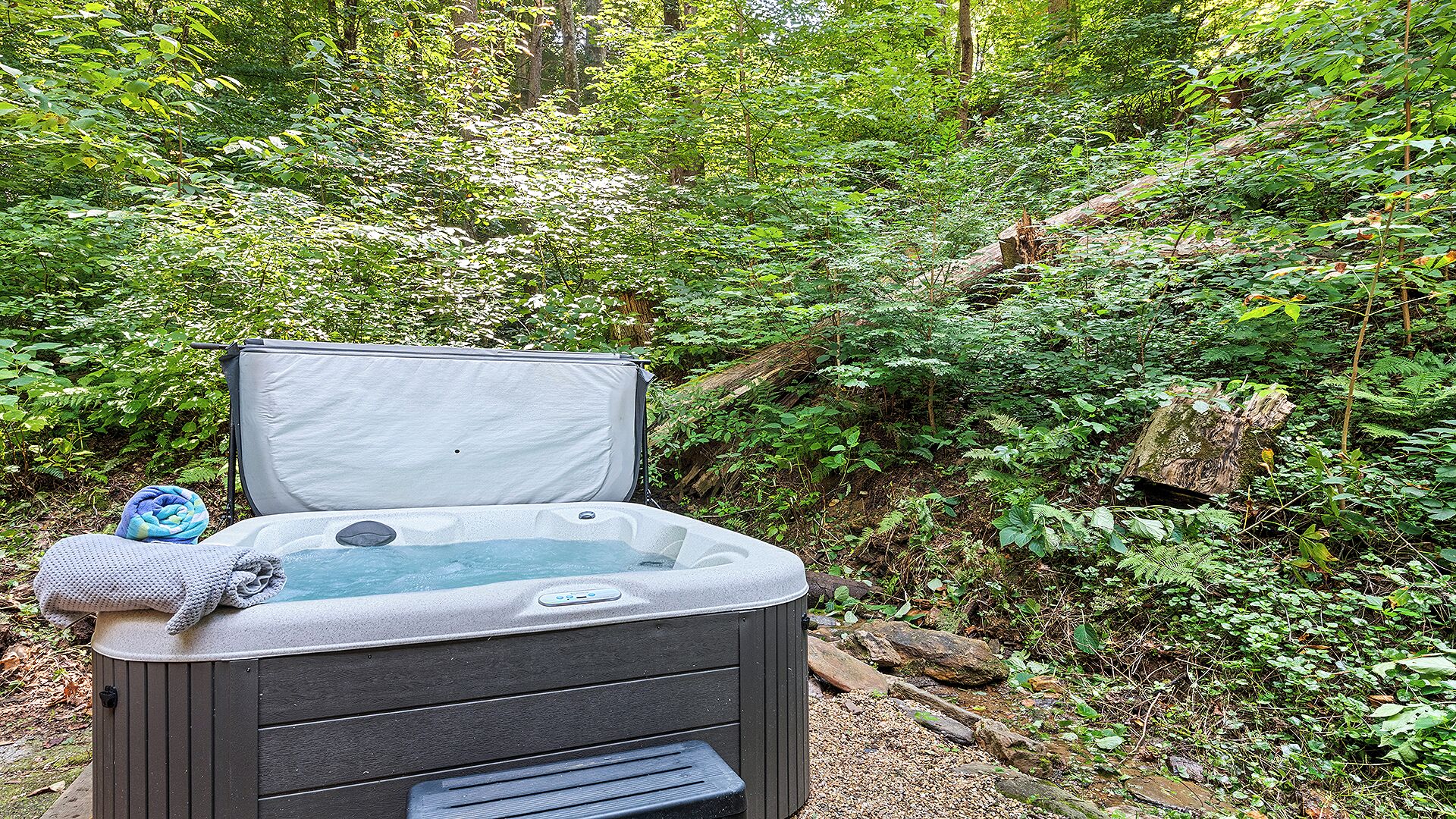 A hot tub in a forested area with a bench and towels.