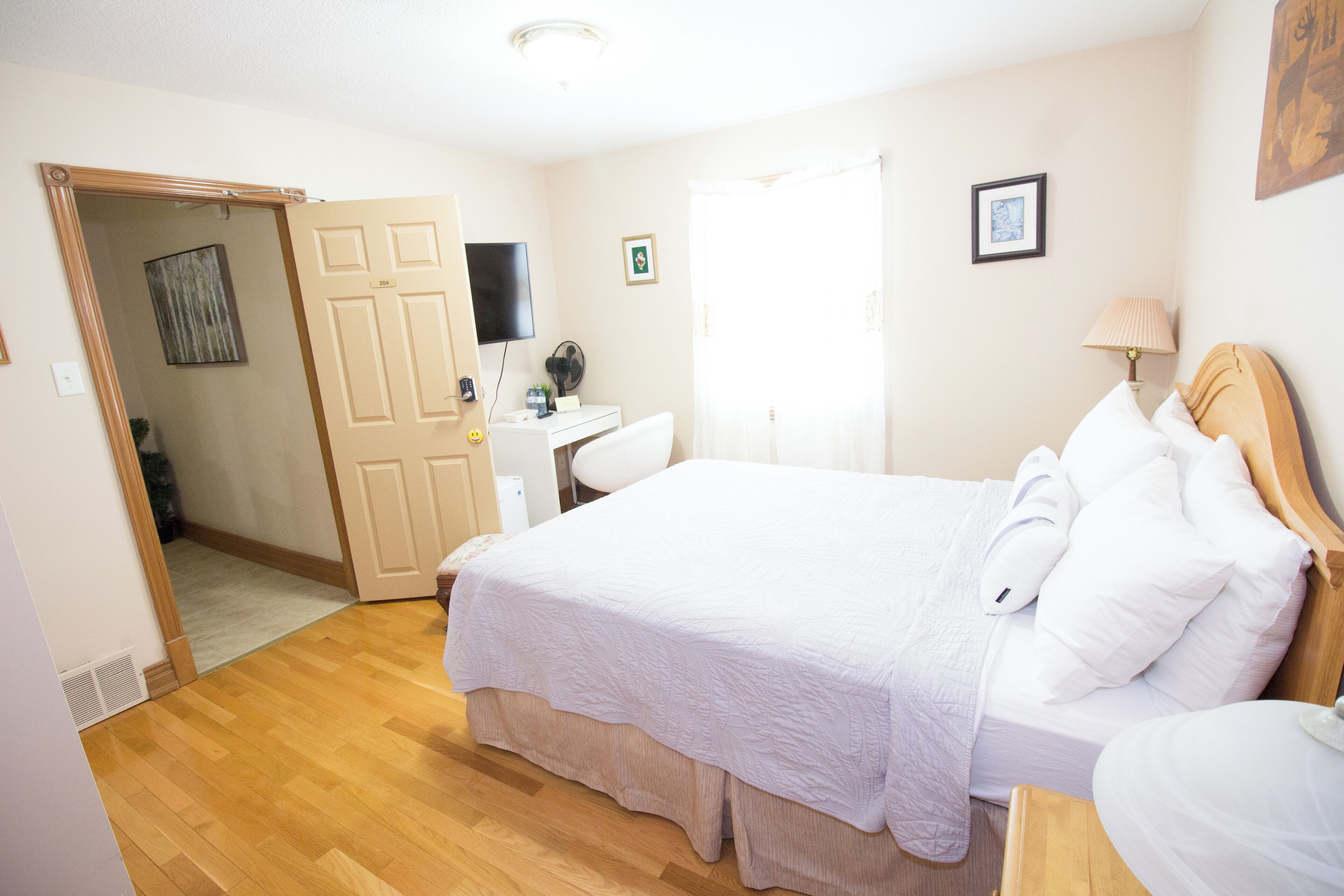 Una camera da letto con un letto, una scrivania, una sedia, una televisione e una finestra con tende.
