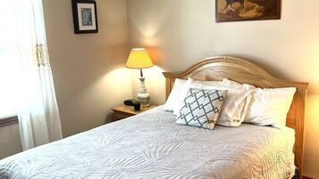 A neatly made bed with a white quilt, a bedside lamp, a framed picture on the wall, and a wooden headboard.