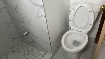 Un bagno con il water, una doccia e un pavimento piastrellato.