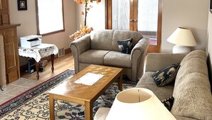 A living room with a sofa, a coffee table, a lamp, a fireplace, and a door with an exit sign. - Anna's Bed & Breakfast (Niagara Falls)