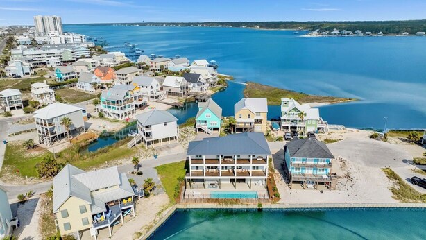 Vue aérienne d’un quartier résidentiel situé sur la côte, avec des maisons, une piscine et une plage.