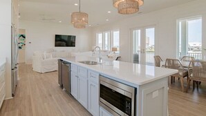Une cuisine spacieuse avec des meubles blancs, un grand îlot central et un coin repas doté de chaises en osier.