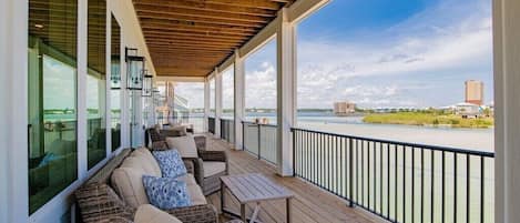 Une terrasse extérieure couverte, aménagée avec des meubles en osier et offrant une vue sur une rivière.