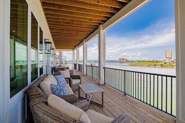 A covered outdoor deck with wicker furniture and a view of a river.