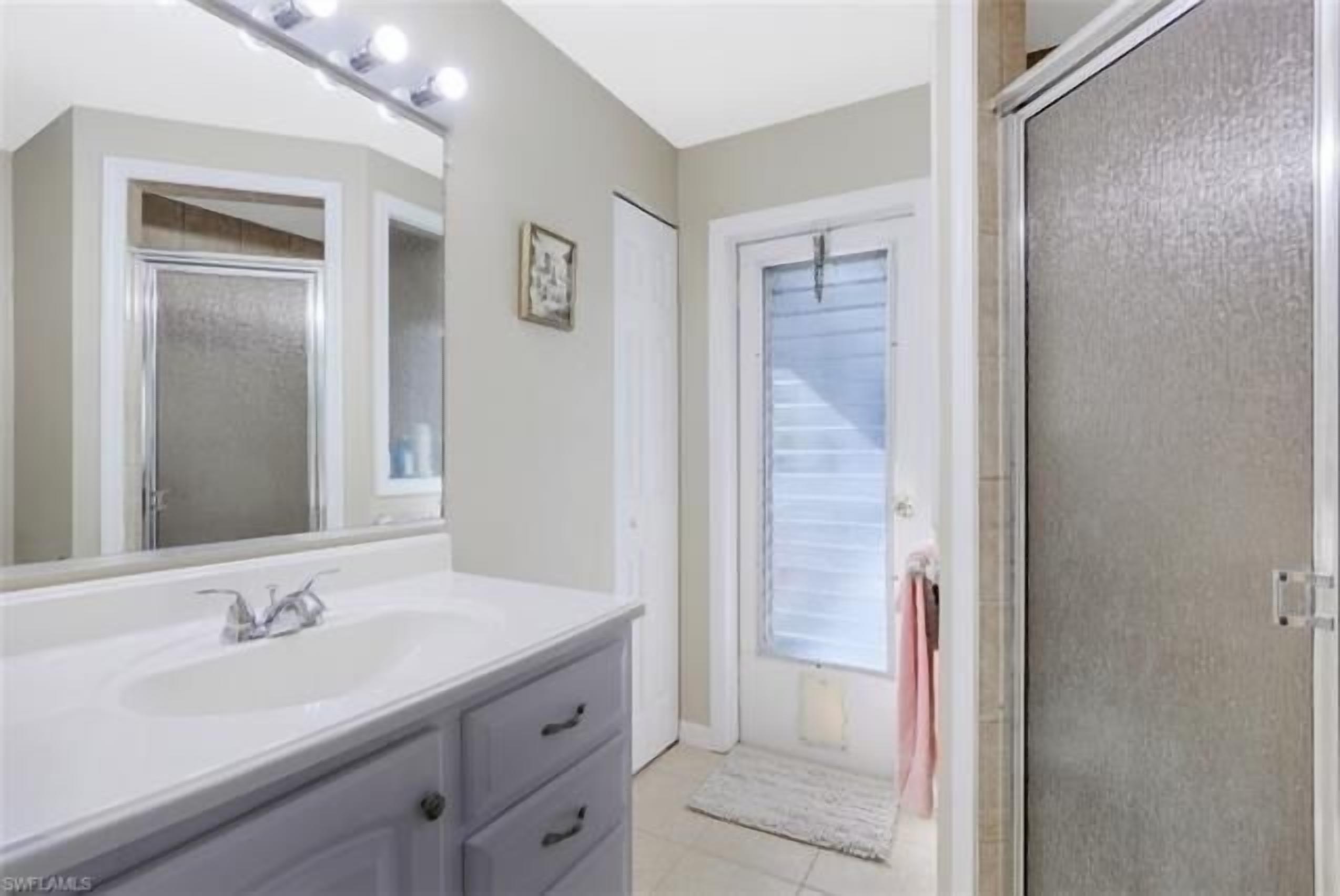 A bathroom with a large mirror, a white sink, and a shower area.
