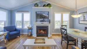 A living room with a fireplace, a television mounted above it, and a dining area with a glass table.