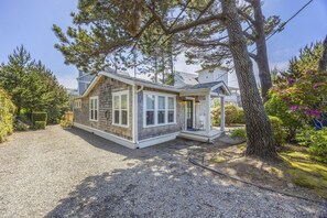 Une maison avec une allée en gravier, un porche abrité et un grand arbre au premier plan.
