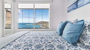 A bedroom with a large window offering a view of the sea and a distant coastline. - Home2Book Blue Sea View Patalavaca Beach Apartment (Patalavaca)