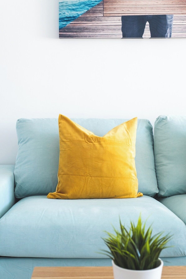 A light blue sofa with a mustard yellow pillow and a small potted plant on a wooden table. - Home2Book Blue Sea View Patalavaca Beach Apartment (Patalavaca)