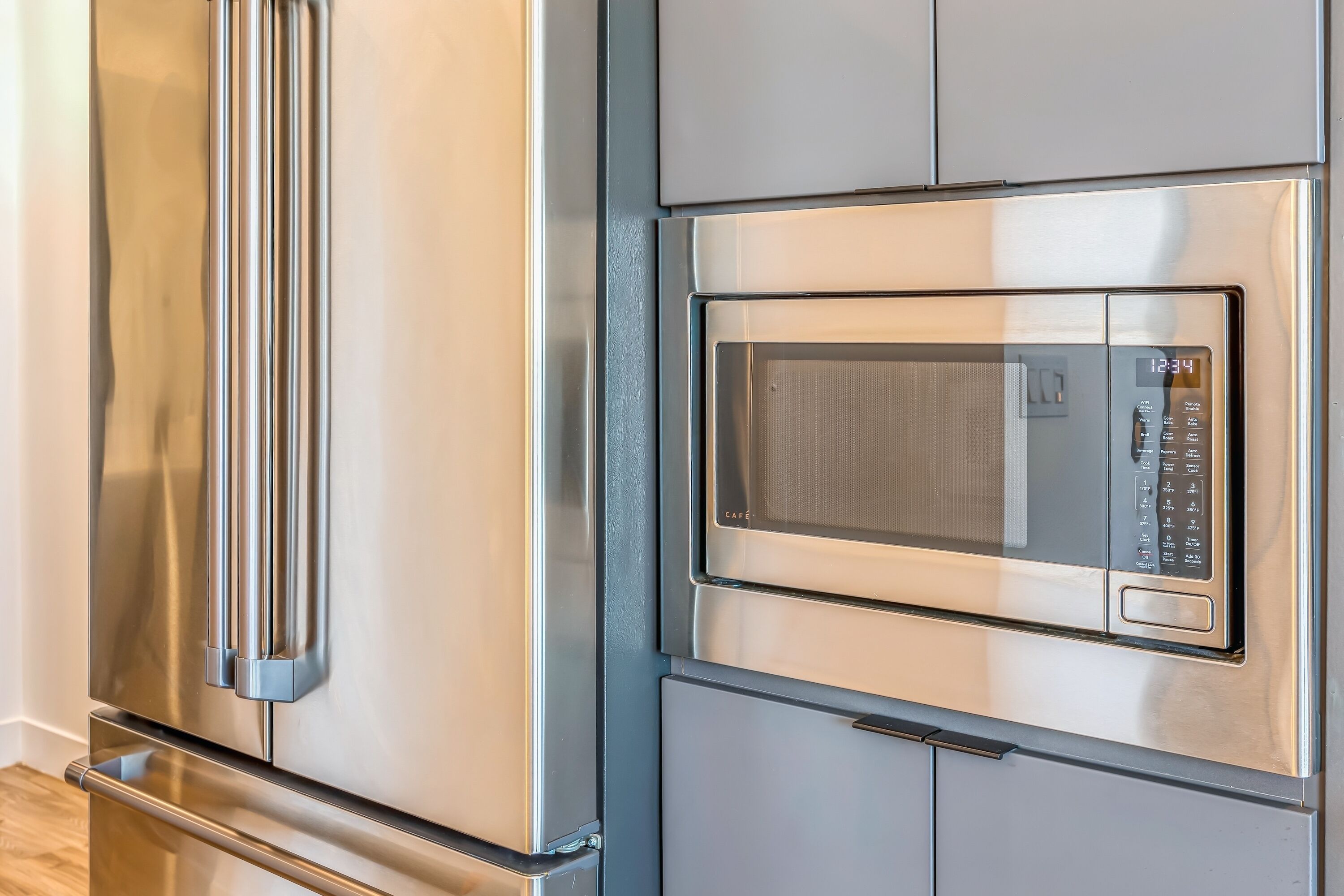 A stainless steel refrigerator and microwave in a kitchen with a wooden floor.