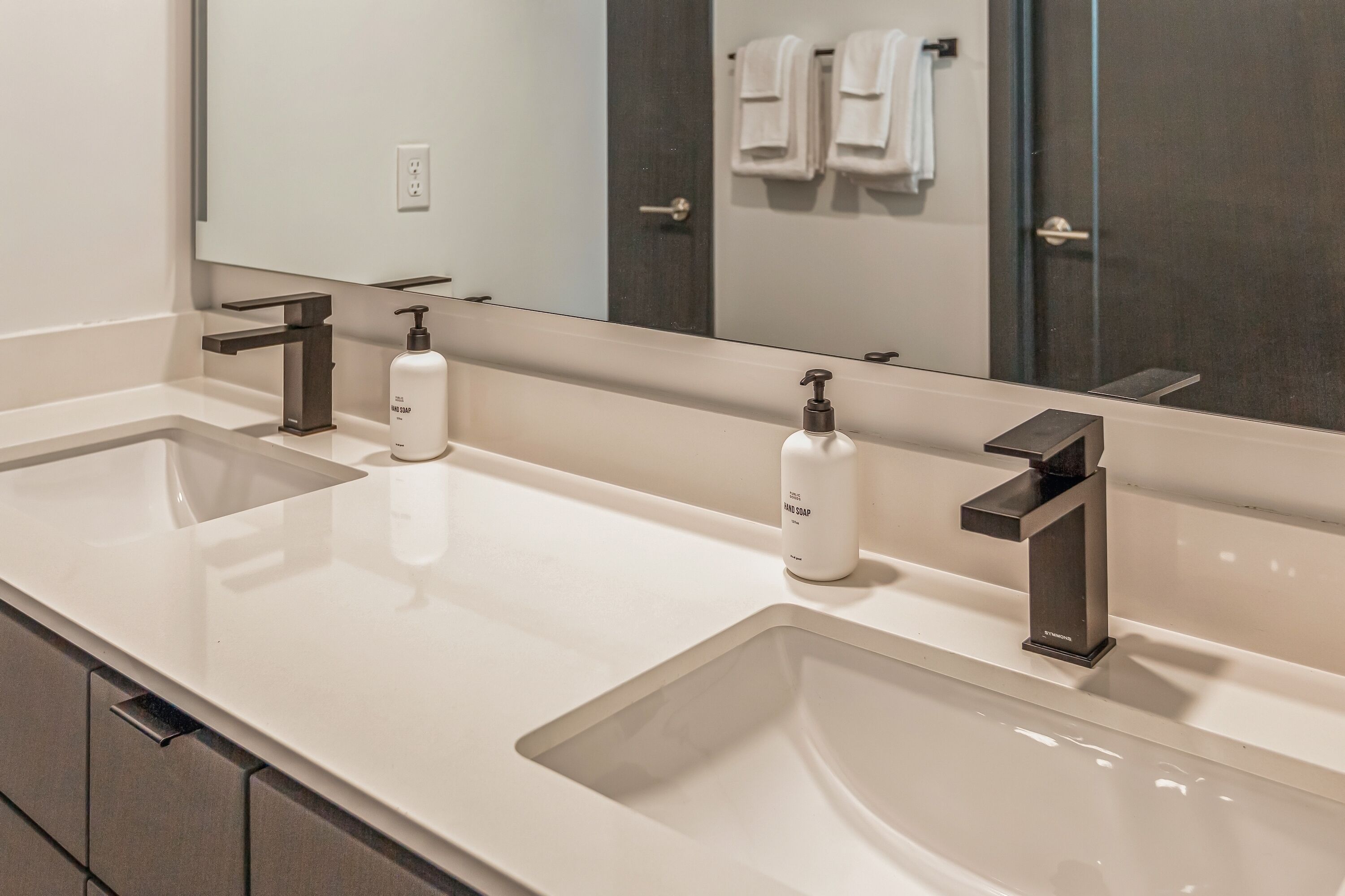 A modern bathroom with two sinks, a large mirror, and a towel rack.
