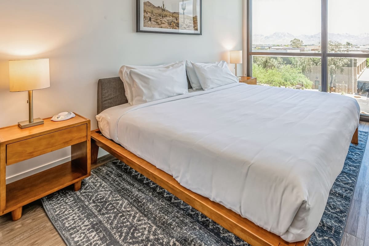 A bedroom with a large bed, two bedside tables with lamps, a rug, and a framed picture on the wall.