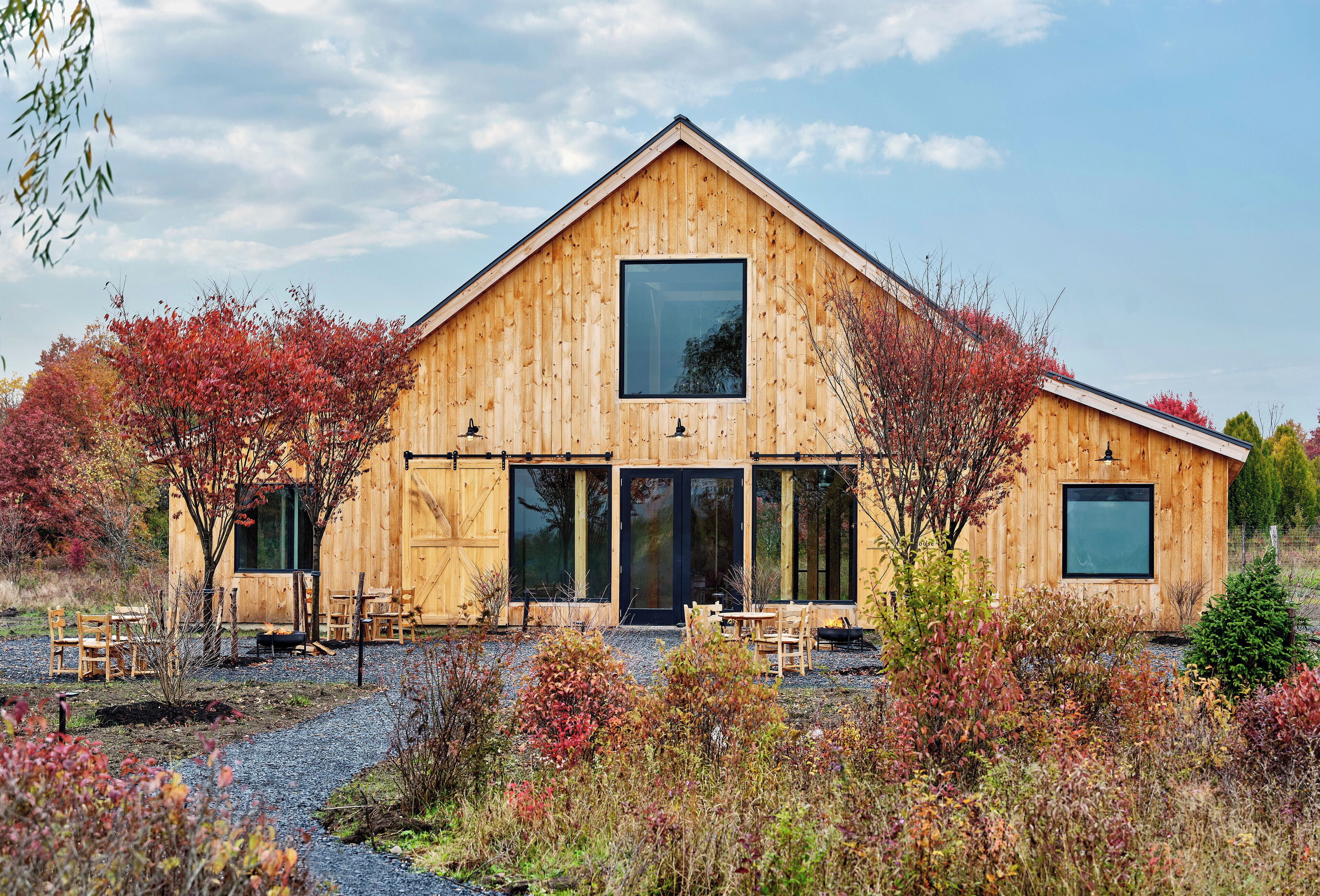 A wooden barn-style building with large windows and a gravel driveway.