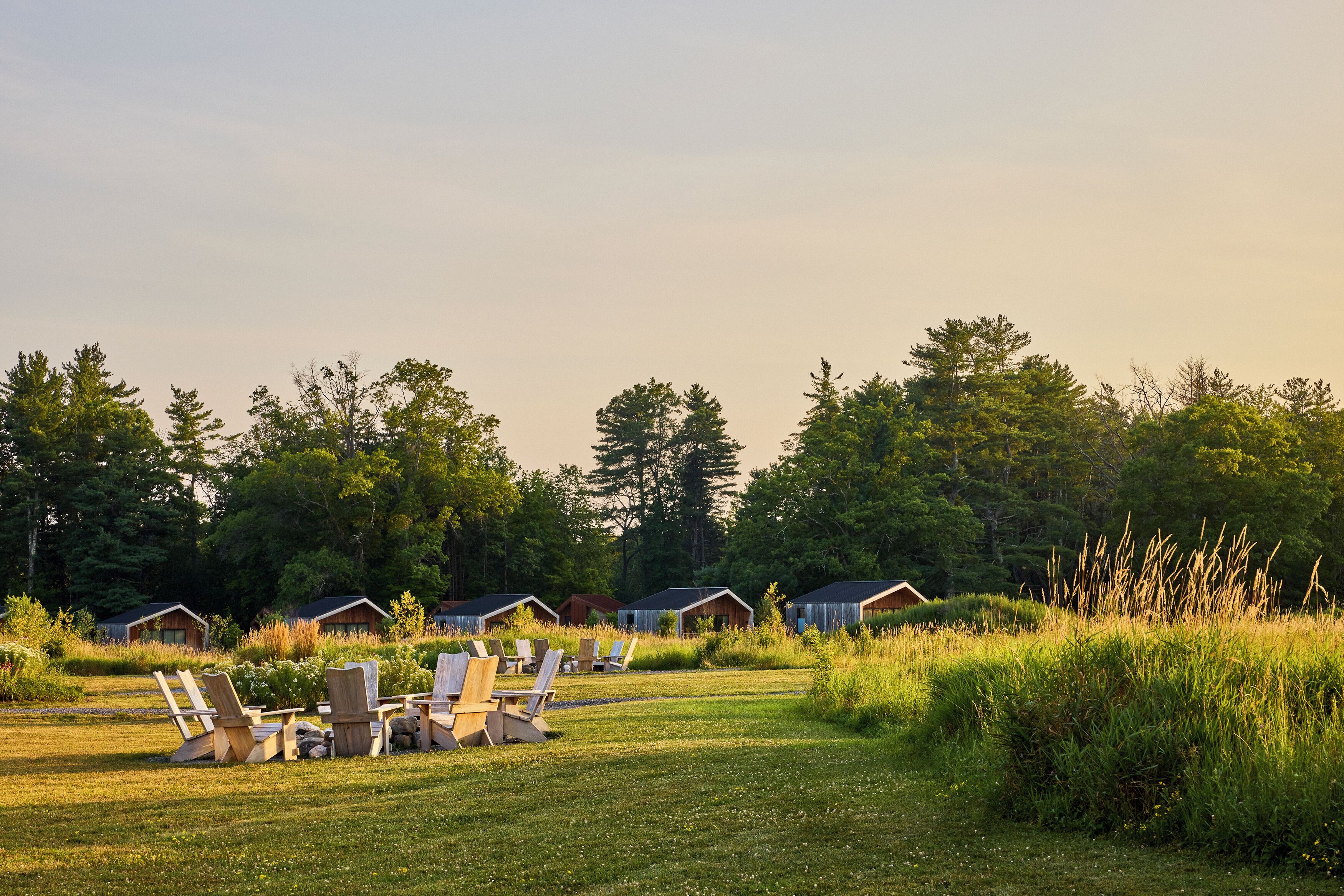 A campground with several wooden cabins, outdoor seating areas, and a grassy field.