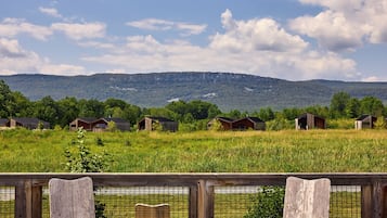 Un patio con dos sillas de madera y una pequeña mesa, con vista a un campo cubierto de césped y varias cabañas de madera a lo lejos.