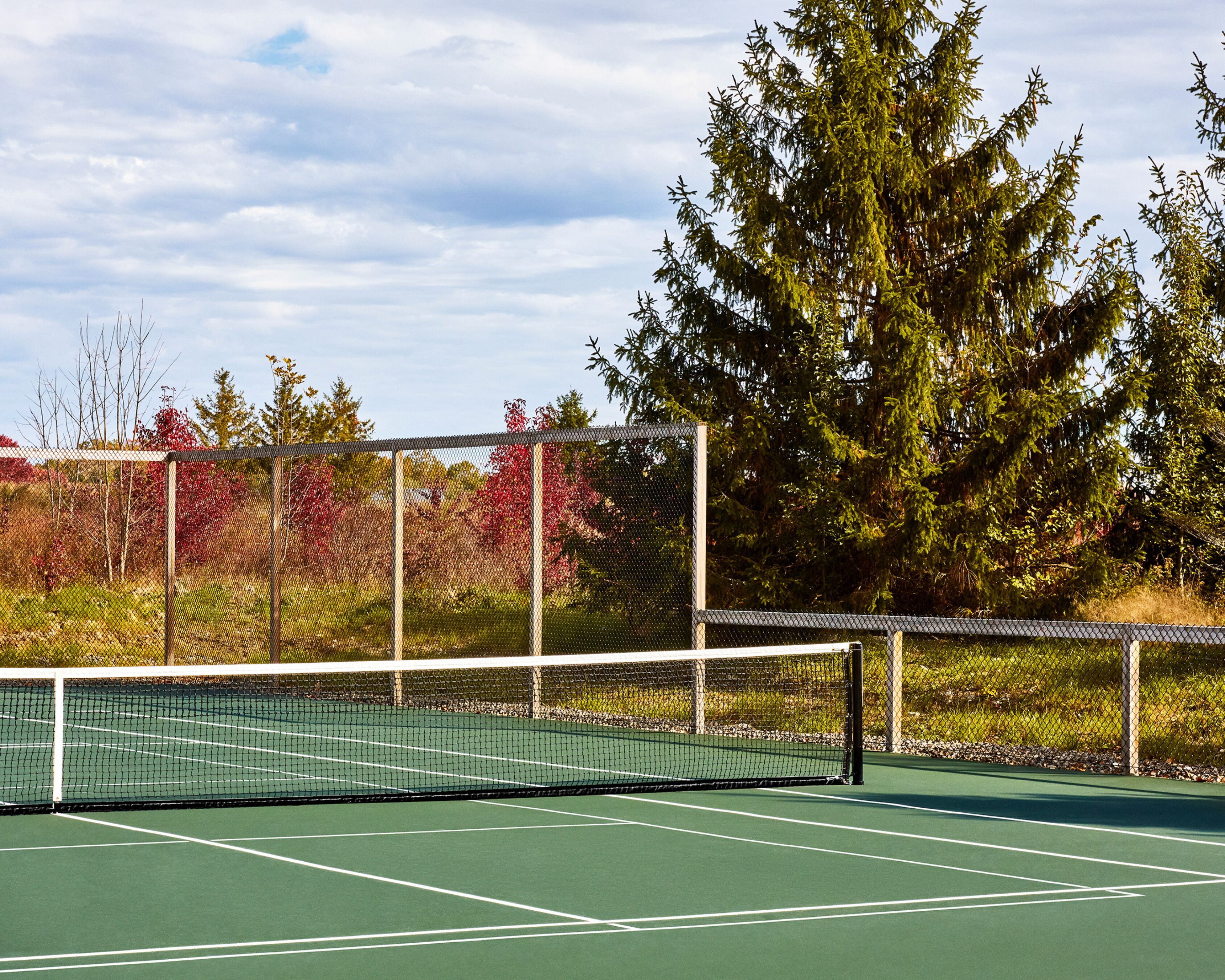 A tennis court with a net, surrounded by trees and a fence.