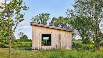 A rustic wooden cabin with a large window, surrounded by lush greenery and trees.