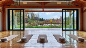 Una habitación amplia con vigas de madera, ventanas grandes y vista a un lago rodeado de árboles.