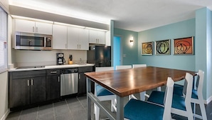 A modern kitchen with white cabinets, a stainless steel microwave, and a black refrigerator. There is a wooden dining table with blue chairs. - Beautiful Daytona Beach Oceanfront 2 Bedroom Condo (Daytona Beach)